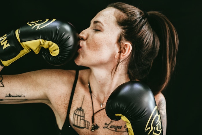 A woman with tattoos and her hair in a pony tail kissing her boxing gloves