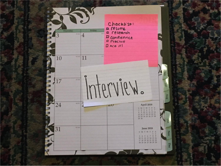 A planner with a pink stick note of helpful tips for an interview and a flashcard on top that reads "Interview"
