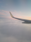 A plane flying through clouds with a sunset in distance.