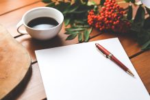 A still life of a coffee cup, a paper and pen.